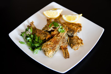 Fried fish on a white plate. Grilled crucian with lemon and parsley.