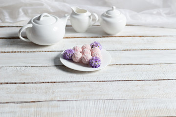 Pink sweet cookies with coconut flakes, fresh primula flowers in plate, tea crockery  on white wooden background