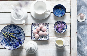 Pink sweet energy balls with coconut flakes in plate, primula and muscaria flowers, tea crockery  on white wooden background