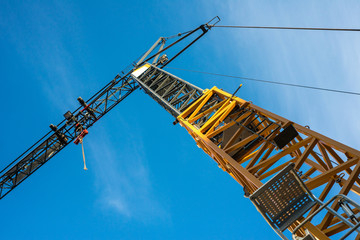 Gelber Turmkran auf einer Baustelle, von unten fotografiert, mit blauem Himmel im Hintergrund.