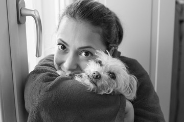 ritratto in b/n ragazza bianca a casa insieme al suo cane maltese che guarda serena