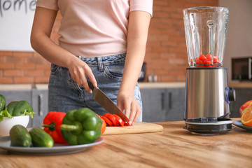 Young woman making smoothie in kitchen at home