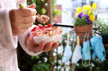 Colazione durante Covid 19. La donna fa colazione tenendo una ciotola con yogurt, cereali e frutti...