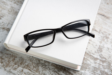 reading glasses resting on a white cover book and a wooden table