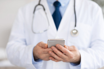 Doctor using smartphone at workplace, messaging with patients