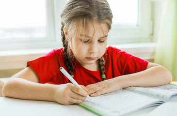 Naklejka na ściany i meble the child is studying at home. Distance learning. A girl sits by the window and does homework.