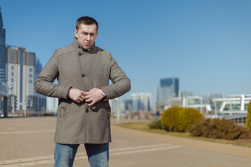 A young adult man in a gray coat walks along a city street on a sunny day in spring