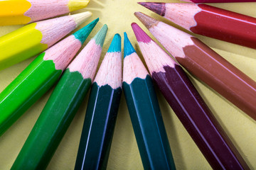 Fototapeta premium Colored pencils arranged in a circle, macro photographed from above on a yellow background.