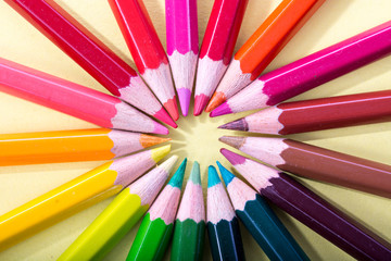Naklejka premium Colored pencils arranged in a circle, macro photographed from above on a yellow background.