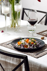 Photo of a home cozy supper with glass of red wine and salad from fresh eco vegetables on black plate indoors