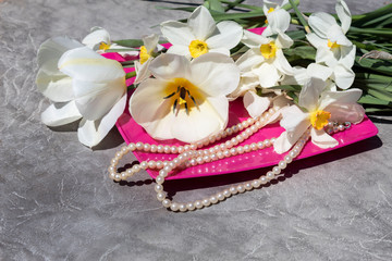 On a pink plate are white daffodils, tulips and beads.