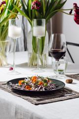Photo of a home cozy supper with glass of red wine and salad from fresh eco vegetables on black plate indoors