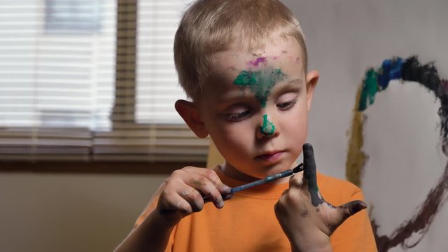 Cute child (Caucasian boy) is having fun, painting his finger.  Kids dirty face and hands after art activities, close up. Fun activity for kids indoor, parenting  concept