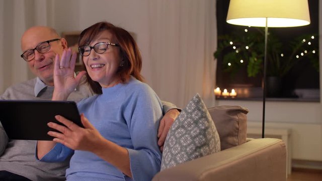 technology, old age and people concept - happy smiling senior couple with tablet pc computer having video call at home in evening