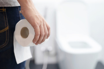Man suffers from diarrhea hand hold tissue paper roll in front of toilet bowl. constipation in bathroom. Treatment stomach pain and Hygiene, health care concept.