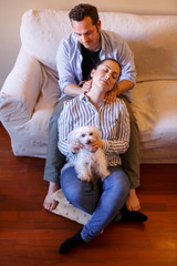 ragazzo in camicia seduto sul divano fa dei massaggi al collo alla sua compagna seduto di fronte a lui sul pavimento