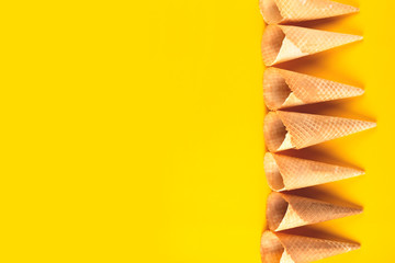 Waffle cones for ice cream on a bright yellow background. The concept of a cooling summer dessert.