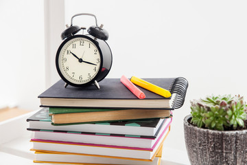 Alarm clock and felt-tip pens on a stack of books and a ceramic pot with succulent. Concept - back...
