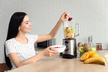 Young woman making fruit smoothie in kitchen at home