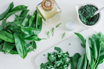 Frische grüne Bärlauchblätter und ein Glas mit Pesto und Küchenutensilien auf weißem...