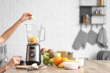 Young woman making fruit smoothie in kitchen at home