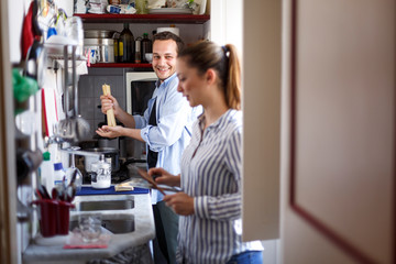 Fototapeta na wymiar Coppia di fidanzati scherza e ride divertita mentre prepara il pranzo in cucina