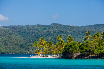 
Sea Caribbean landscape in Dominican republic with palm trees, sandy beach, green mountains, rocks, blue sky and turquoise water 