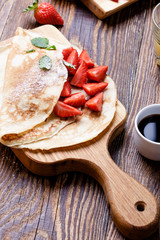 Crepes with fresh strawberries on wooden cutting board