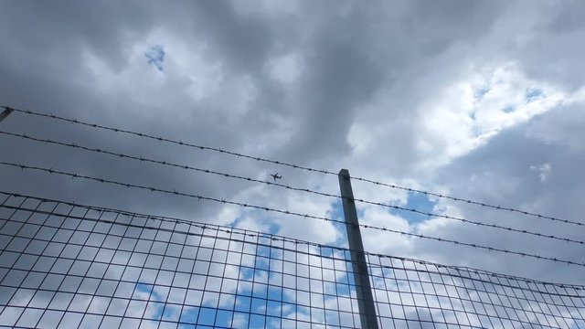 A plane flies past a barbed wire fence
