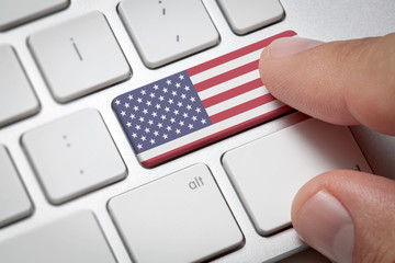Online International Business concept: Computer key with the United States of America flag on it. Male hand pressing computer key with America flag.