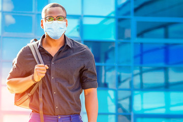 handsome trendy African American university lecturer male with glasses in stylish clothes black shirt with a backpack on the shoulders stand background of the blue windows