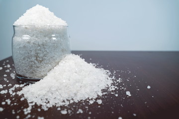 white crystalline salt in a transparent glass jar scattered on a brown table