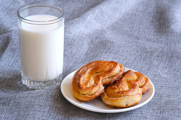 Milk in a glass on a background of burlap. Freshly baked sweet rolls on a saucer. Natural product. Isolated background. Milk drink. Splash of milk.
