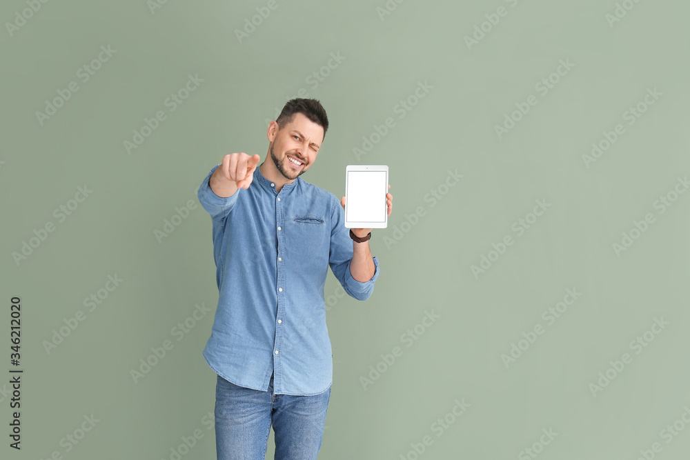 Poster handsome man with tablet computer pointing at viewer on color background
