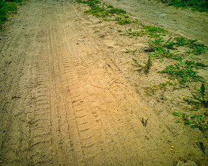 Abstract high contrast close-up of rocky gravel driveway road tire imprint in brown sand with grass...