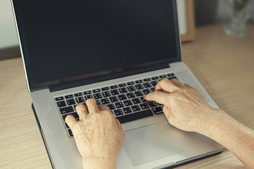 Old woman hand with wrinkle working on laptop computer at home