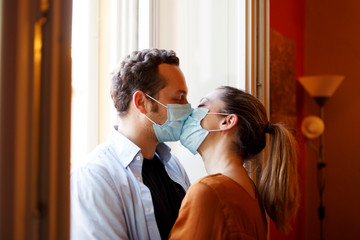 coppia di fidanzati con la mascherina chirurgica  si danno un caloroso bacio a casa.