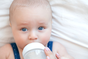 Beautiful baby eating milk from bottle in white bedroom on white background