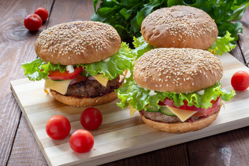 Photo homemade burgers with beef, onions, tomatoes, lettuce, cheese and spices. Fresh burgers on a wooden Board with cherry tomatoes.