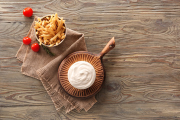 Bowls with tasty sour cream and french fries on table