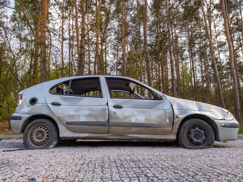 Low angle side view of dumped and damaged car wreck at a car park in a forest.