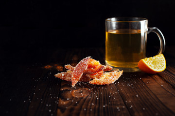 Orange peels in sugar. Candied fruit from orange. Orange marmalade on a wooden brown table with a black background. Tea with sliced ​​orange. Empty space for text.