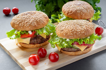 Photo homemade burgers with beef, onions, tomatoes, lettuce, cheese and spices. Fresh burgers on a wooden Board with cherry tomatoes.