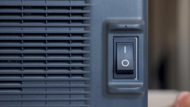 finger of a person presses turns on and off on a black plastic button a swing printer device with a radiator