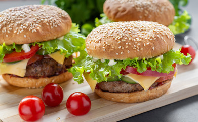 Photo homemade burgers with beef, onions, tomatoes, lettuce, cheese and spices. Fresh burgers on a wooden Board with cherry tomatoes.