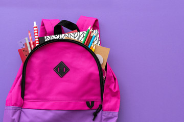 Back to school concept. Backpack with school supplies on purple background. Top view. Copy space