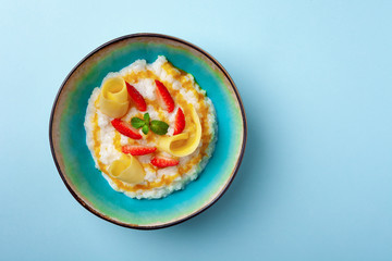 Bowl of milk rice porridge with strawberries, mangoes, honey, mint