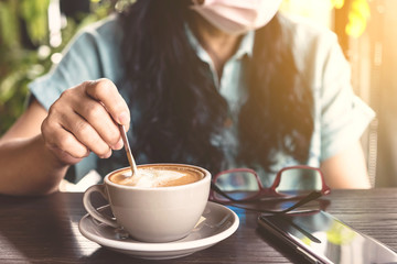 Woman with medical face mask drinking coffee in her house alone during corona virus or COVID-19 quarantine, Physical distancing for protect Covid-19 concept. Selective focus.