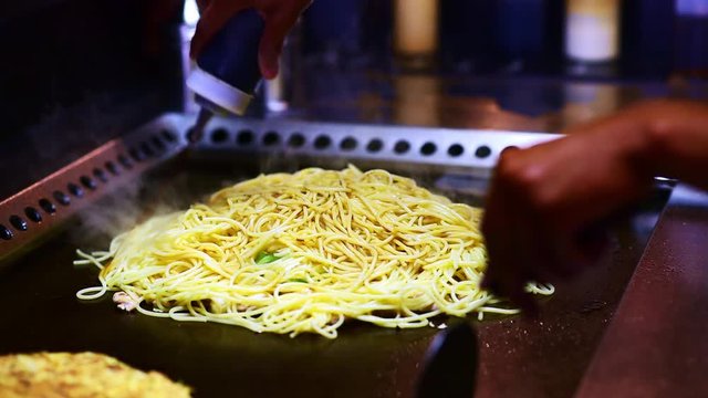Chef pours Worcestershire or soy sauce on spagetti or yakisoba, vegetable and flambeed chicken strips for Asian Chicken and Vegetables Stir Fry noodles or traditional Japanese Okonomiyaki 