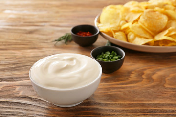 Bowl with tasty sour cream and potato chips on table